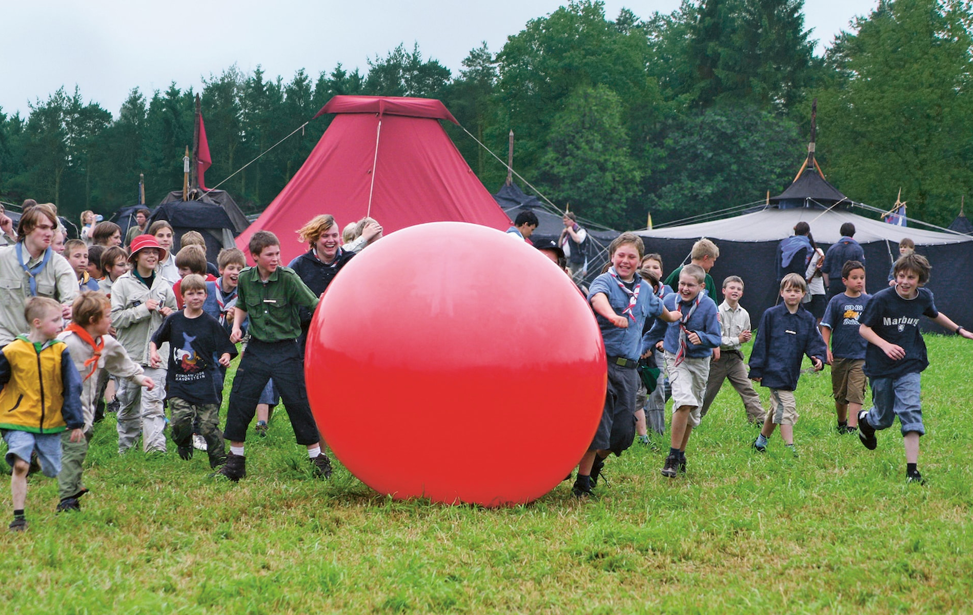 Kinder laufen einem großen roten Ball hinterher